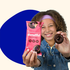 A girl holding up a chocolate dipped donut in one hand and a package of Donutful in the other.