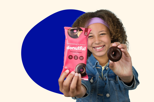A young girl holding a chocolate dipped donut in one hand and a Donutful wrapper in the other