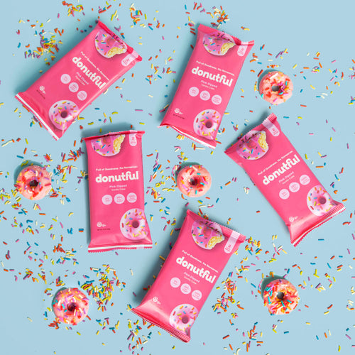 Five packs of pink dipped donuts surrounded by rainbow sprinkles and pink dipped donuts.