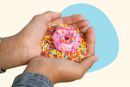 A pink donut resting in the cupped hands of a girl